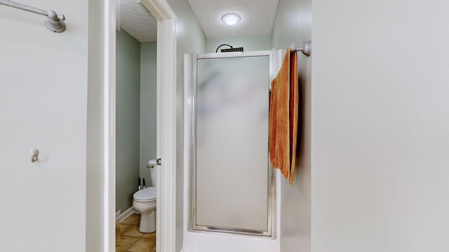 bathroom featuring tile patterned flooring, a shower stall, toilet, and a textured ceiling