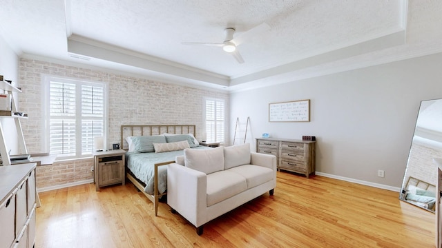 bedroom with light wood-style flooring, brick wall, and a raised ceiling