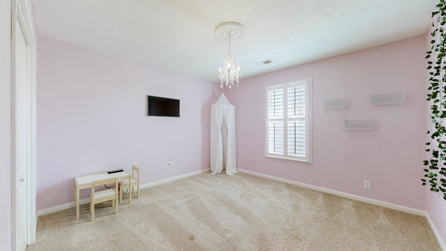 carpeted spare room with baseboards, visible vents, and a chandelier