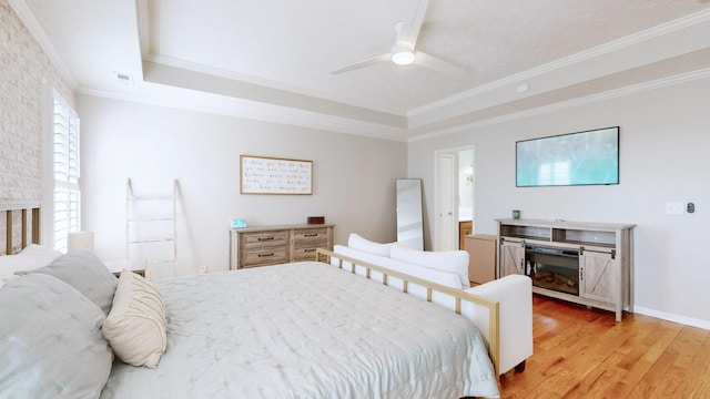 bedroom with light wood finished floors, visible vents, baseboards, ornamental molding, and a raised ceiling