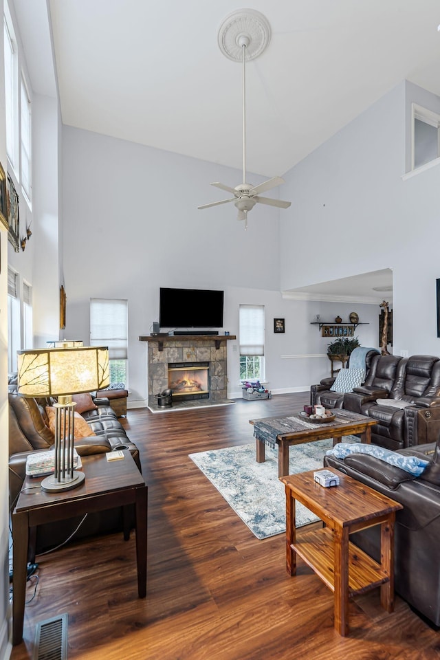 living room with wood finished floors, visible vents, a high ceiling, ceiling fan, and a stone fireplace