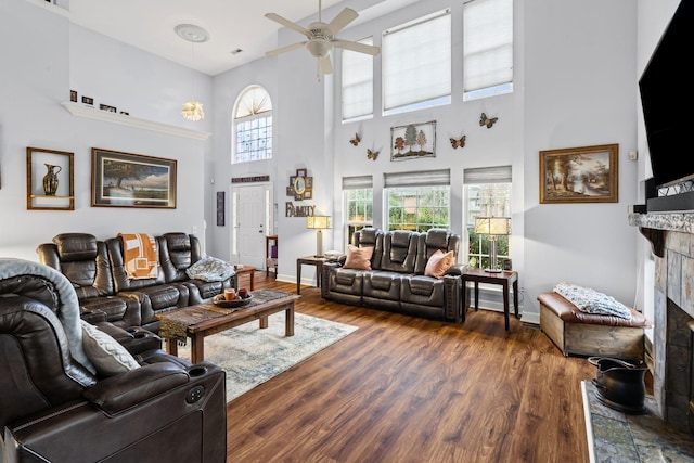 living room featuring dark wood finished floors, a fireplace with raised hearth, baseboards, and ceiling fan