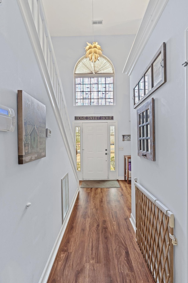 entryway with visible vents, baseboards, a towering ceiling, and wood finished floors