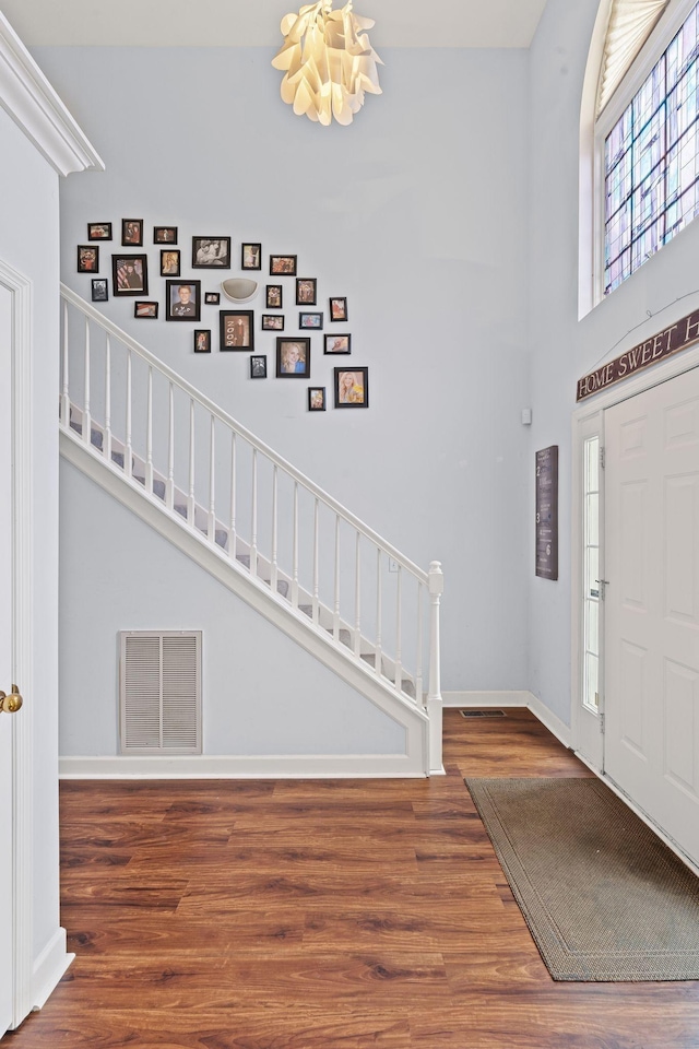 entryway featuring visible vents, baseboards, stairs, a towering ceiling, and wood finished floors