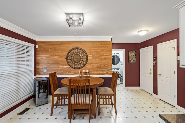 dining area with crown molding, light floors, stacked washer and clothes dryer, and wood walls