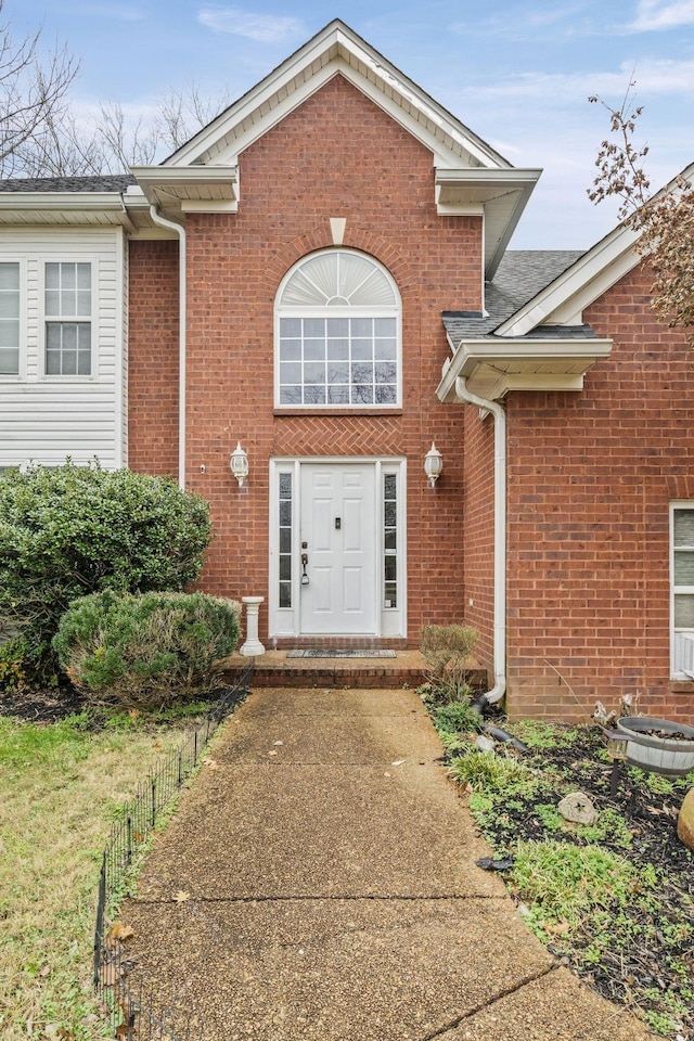 view of exterior entry featuring fence and brick siding