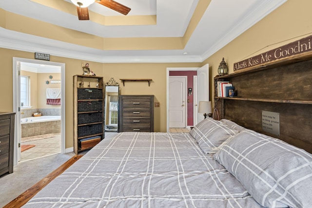 carpeted bedroom with ceiling fan, ensuite bath, a tray ceiling, and ornamental molding