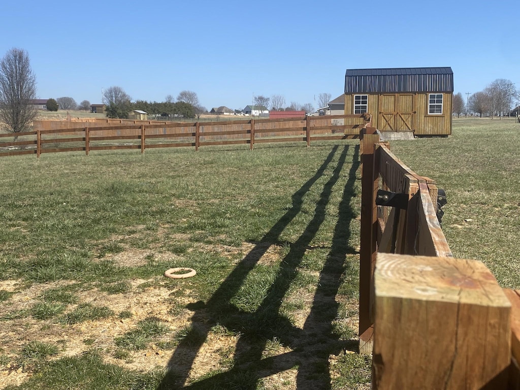 view of yard featuring a rural view, a storage unit, an outdoor structure, and fence