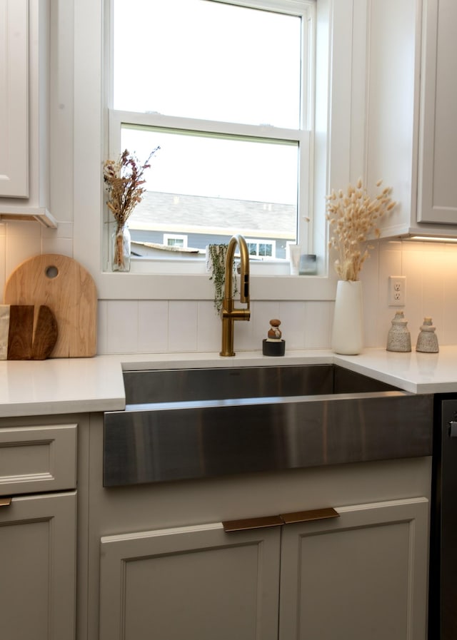 interior details featuring decorative backsplash, light countertops, gray cabinets, and a sink