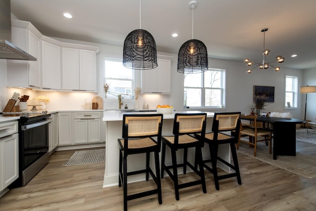 kitchen featuring a wealth of natural light, light wood-type flooring, electric range, white cabinetry, and wall chimney exhaust hood