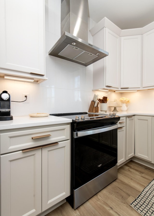 kitchen featuring tasteful backsplash, wall chimney range hood, light countertops, electric stove, and light wood-style floors