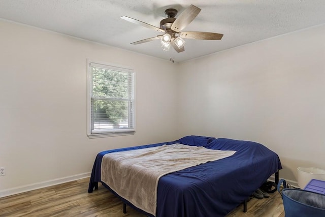 bedroom with ceiling fan, a textured ceiling, baseboards, and wood finished floors