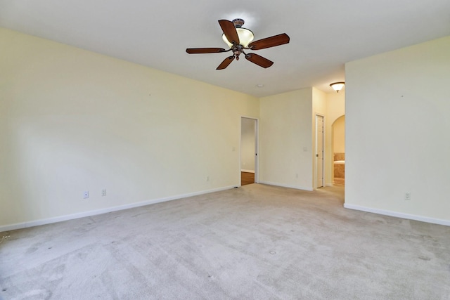 carpeted spare room featuring arched walkways, a ceiling fan, and baseboards