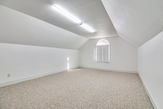 additional living space with light colored carpet, a textured ceiling, baseboards, and lofted ceiling