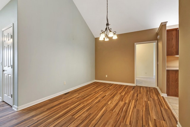 unfurnished dining area featuring lofted ceiling, wood finished floors, baseboards, and a chandelier