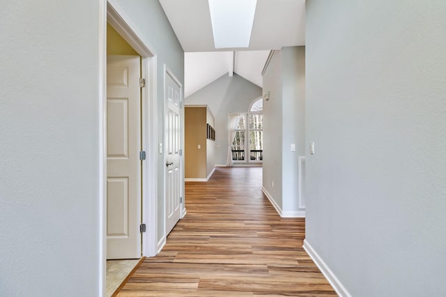 hall with visible vents, vaulted ceiling with skylight, light wood-type flooring, and baseboards