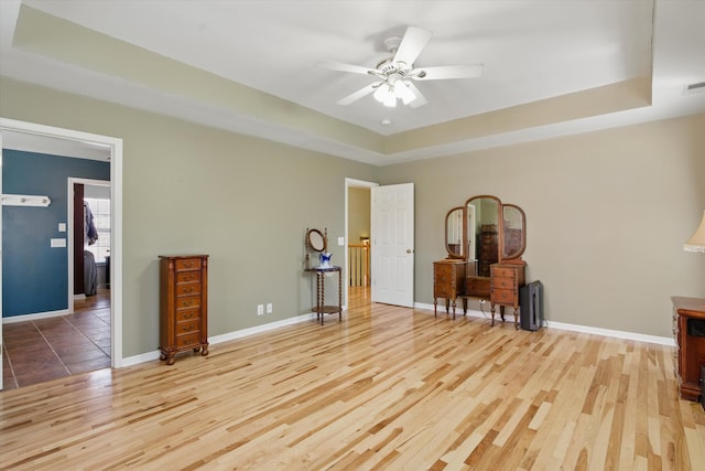 interior space with ceiling fan, a raised ceiling, baseboards, and wood finished floors