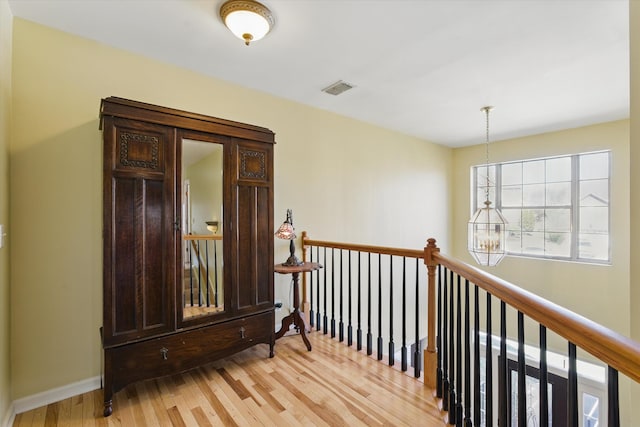 hallway with light wood finished floors, visible vents, baseboards, a chandelier, and an upstairs landing