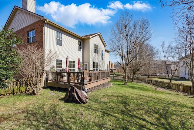 rear view of property featuring a wooden deck, a fenced backyard, a chimney, a lawn, and brick siding