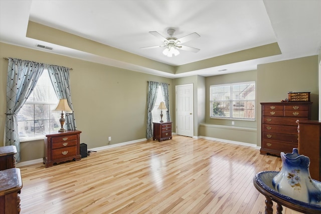 bedroom with visible vents, baseboards, a tray ceiling, and hardwood / wood-style flooring