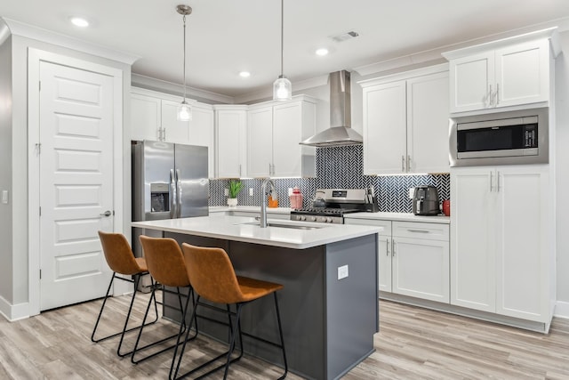 kitchen with an island with sink, a sink, tasteful backsplash, stainless steel appliances, and wall chimney exhaust hood