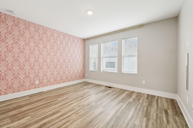 unfurnished room featuring wallpapered walls, visible vents, baseboards, and light wood finished floors