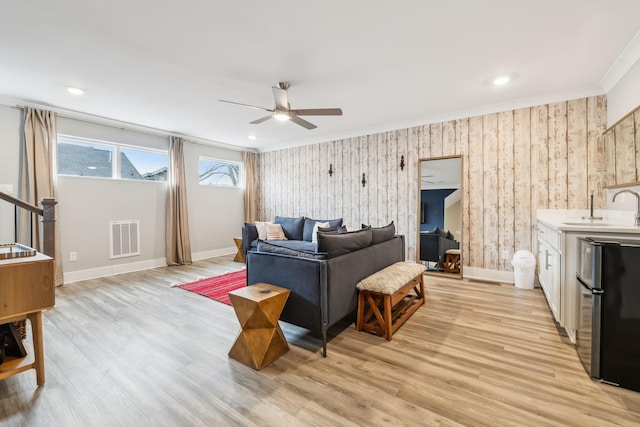 living area featuring visible vents, baseboards, ornamental molding, and light wood-style flooring