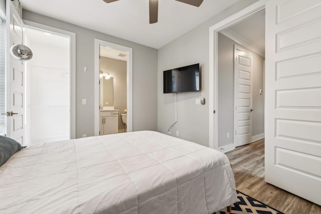 bedroom with baseboards, ensuite bath, wood finished floors, and a ceiling fan