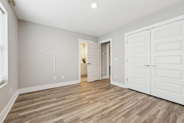 unfurnished bedroom featuring a closet, baseboards, light wood-style floors, and ensuite bathroom