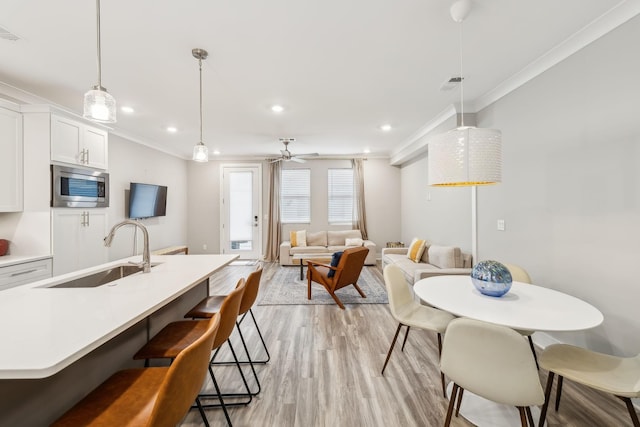 kitchen with stainless steel microwave, ornamental molding, a kitchen breakfast bar, light wood-style floors, and a sink