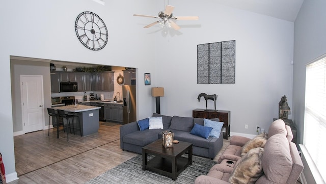 living area featuring ceiling fan, high vaulted ceiling, light wood-type flooring, and baseboards