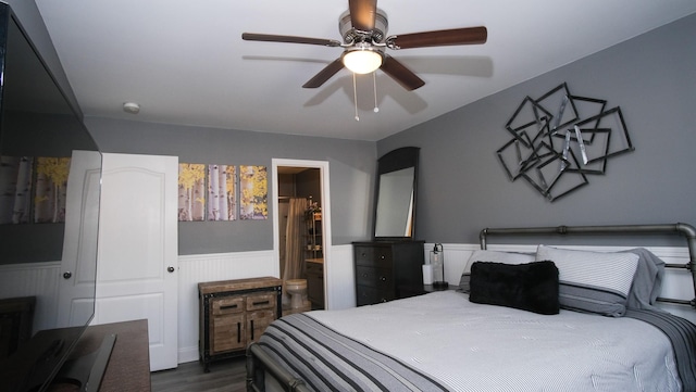 bedroom featuring ensuite bath, dark wood-type flooring, a ceiling fan, and a wainscoted wall