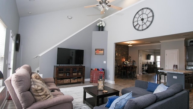 living room featuring crown molding, baseboards, light wood-type flooring, a towering ceiling, and a ceiling fan