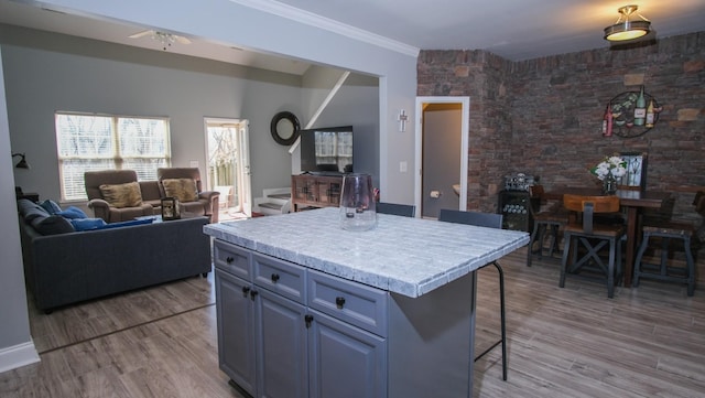 kitchen with ornamental molding, open floor plan, light wood-style floors, a breakfast bar area, and light countertops