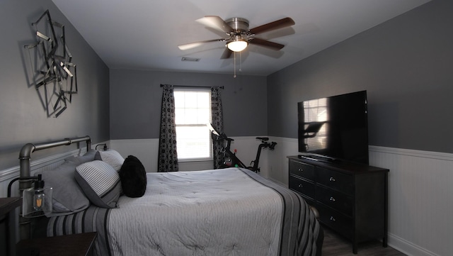 bedroom featuring visible vents, a ceiling fan, and a wainscoted wall