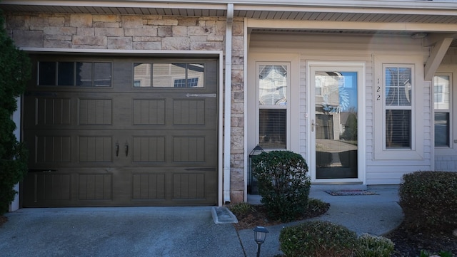 view of exterior entry with concrete driveway, a garage, and stone siding