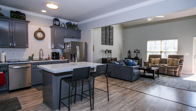 kitchen featuring tasteful backsplash, a center island, a kitchen bar, stainless steel appliances, and a sink