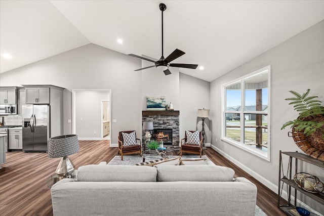 living room featuring a stone fireplace, dark wood-style floors, baseboards, and a ceiling fan