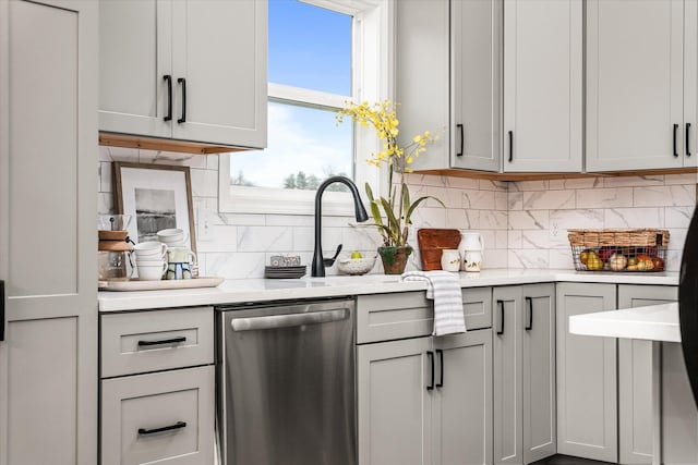 kitchen featuring gray cabinets, a sink, light countertops, dishwasher, and backsplash