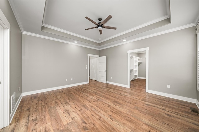 unfurnished bedroom with a tray ceiling, wood finished floors, baseboards, and visible vents