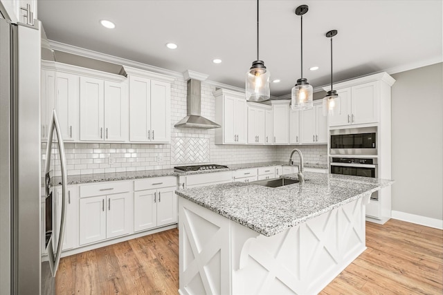 kitchen featuring a sink, ornamental molding, stainless steel appliances, white cabinets, and wall chimney range hood