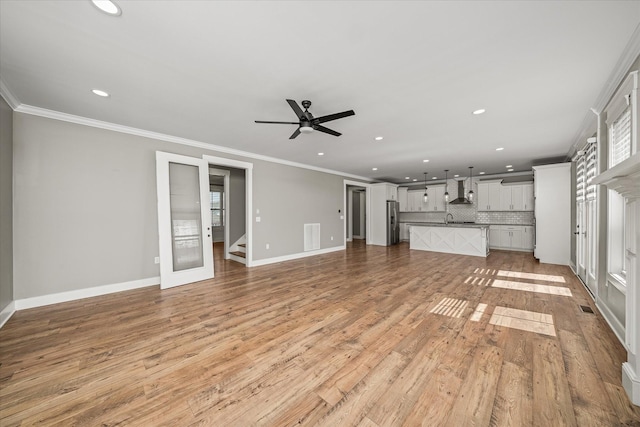 unfurnished living room with baseboards, light wood-type flooring, and ornamental molding