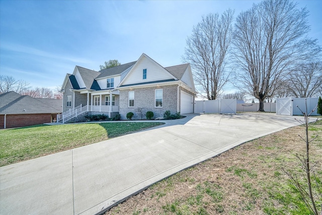 traditional-style house with driveway, a front lawn, a gate, covered porch, and brick siding