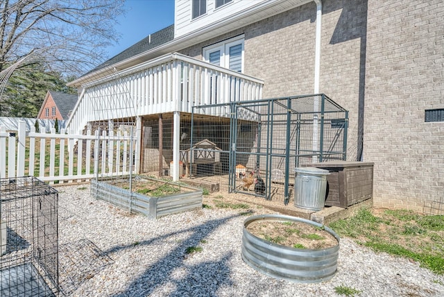 rear view of property featuring a garden, brick siding, an outdoor structure, and fence