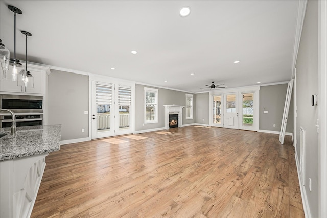 unfurnished living room featuring a glass covered fireplace, baseboards, crown molding, and light wood-style floors