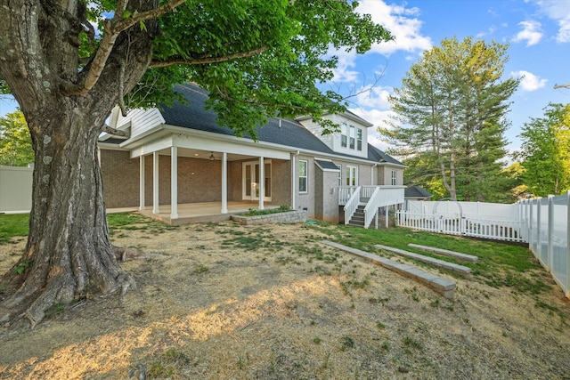 back of property with a deck, a patio area, brick siding, a fenced backyard, and a shingled roof