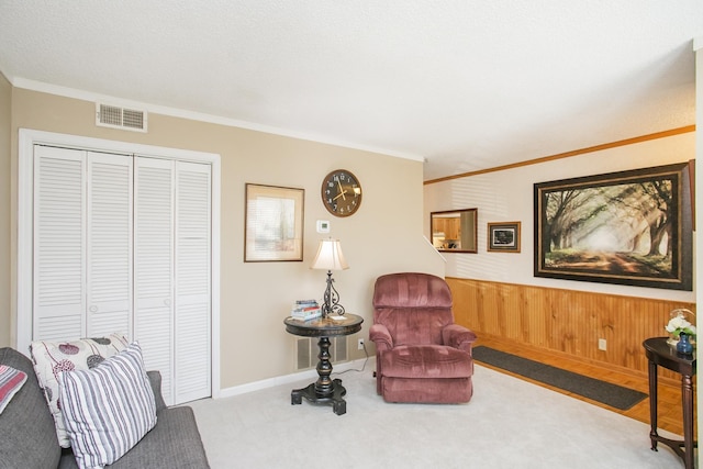 living area featuring carpet, visible vents, wood walls, wainscoting, and crown molding