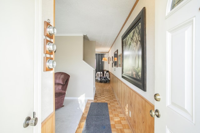 interior space with ornamental molding, a wainscoted wall, wood walls, and a textured ceiling