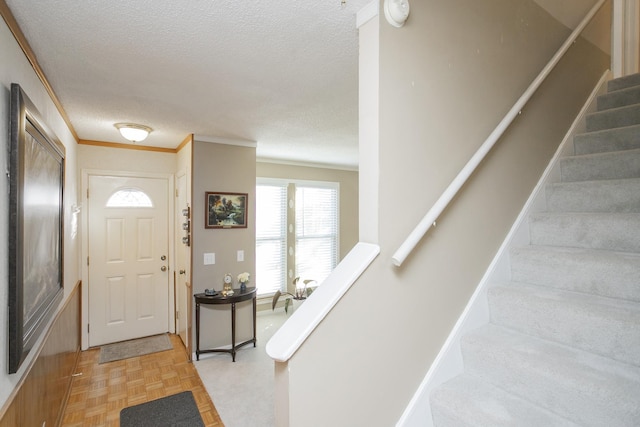 foyer featuring stairway, a textured ceiling, crown molding, and baseboards