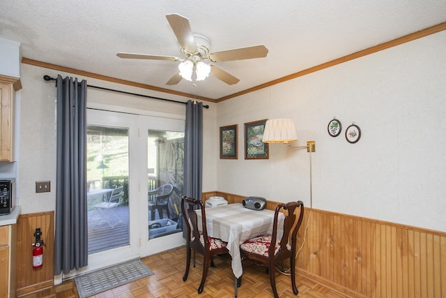 dining room with wooden walls, a textured ceiling, wainscoting, and crown molding